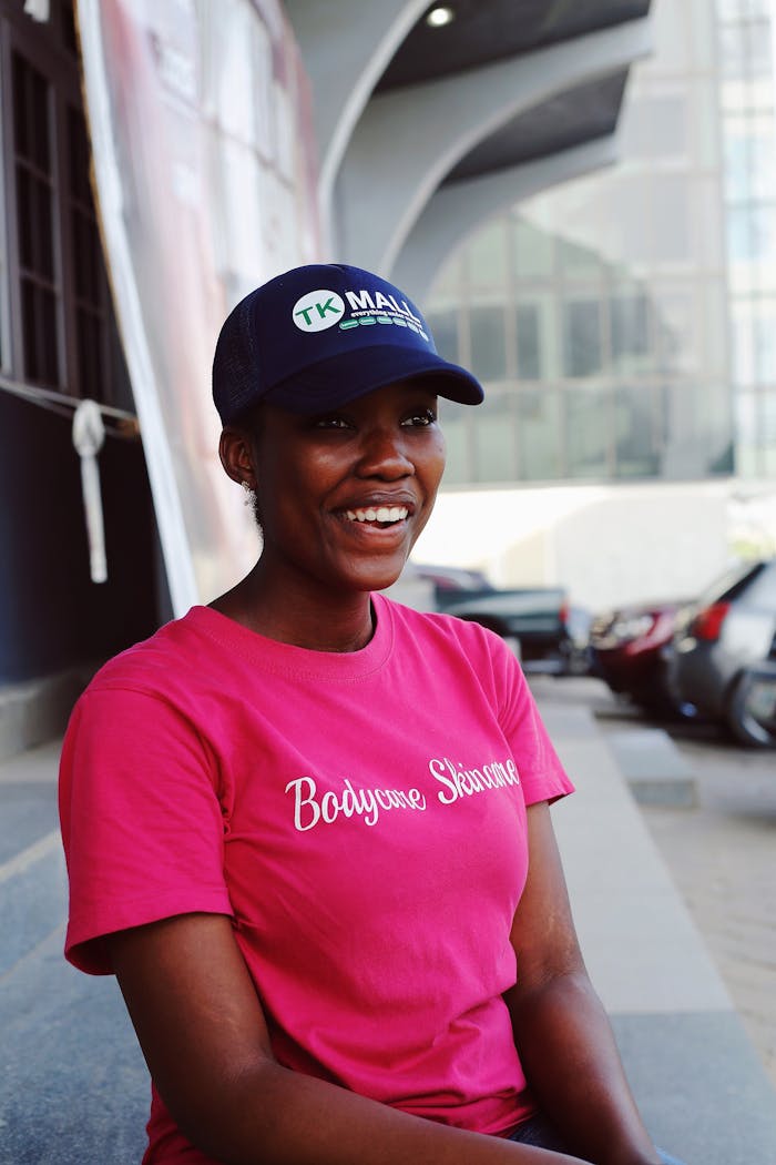 Cheerful African woman sitting outdoors, smiling brightly in a pink T-shirt.