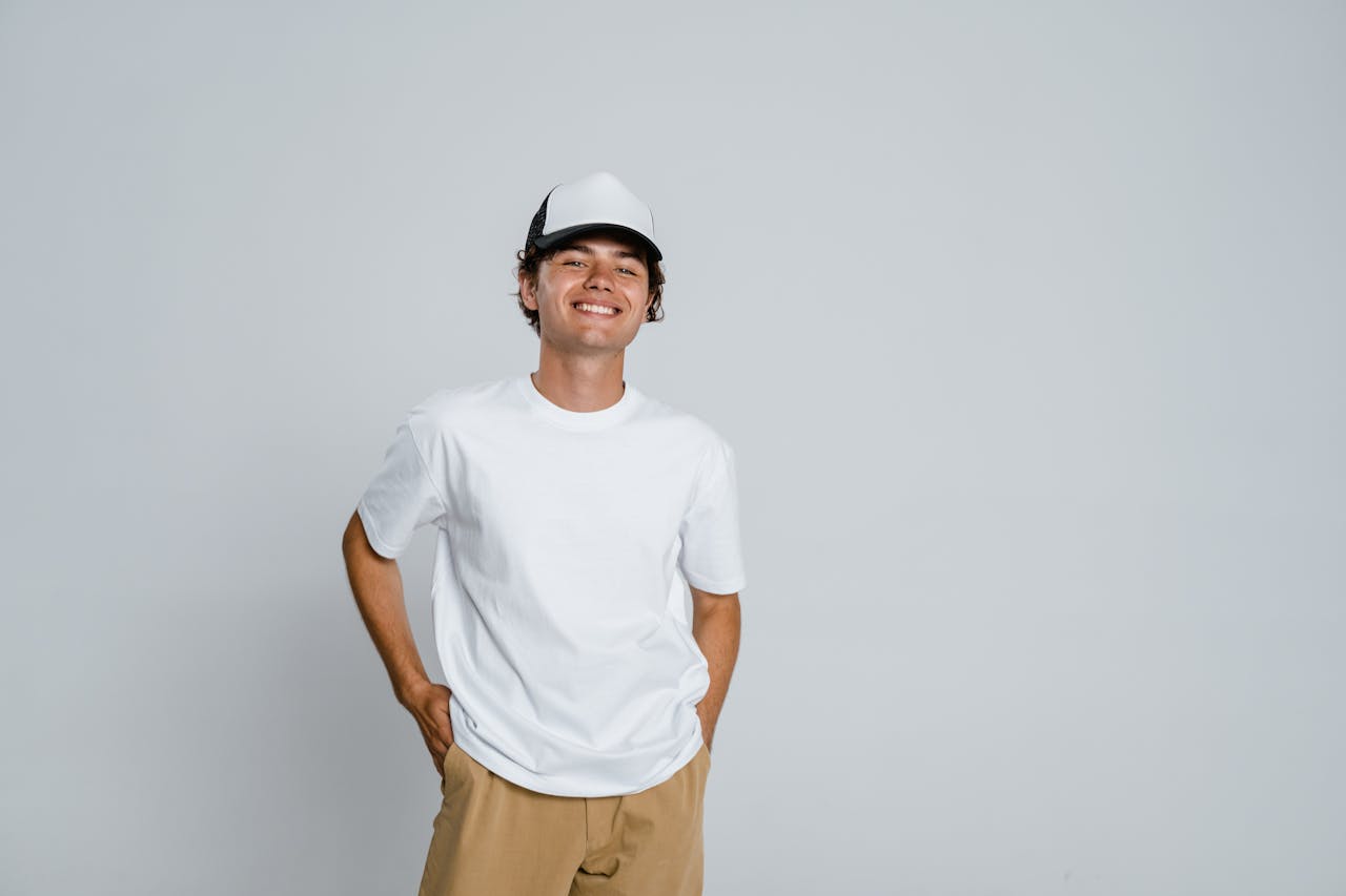 Casual portrait of a smiling man in a white t-shirt and cap against a plain backdrop.